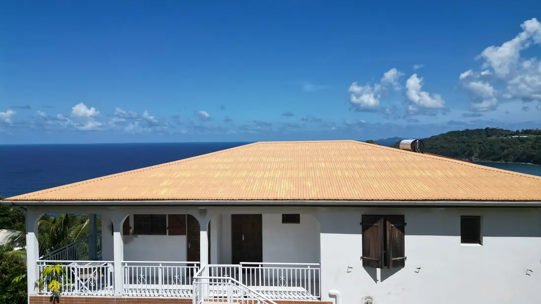 Chantier de toiture réalisé par Mes Primes Rénovations à Le Marigot : maison en surplomb de mer, couverture avant et après reprise