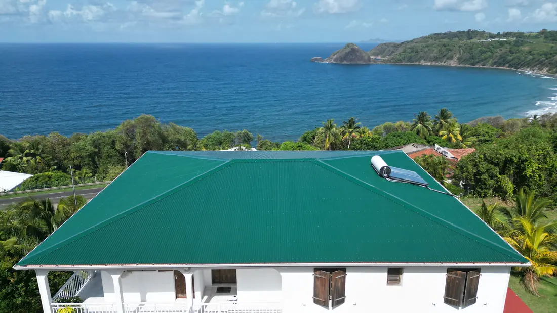 Chantier de toiture réalisé par Mes Primes Rénovations à Le Marigot : maison en surplomb de mer, couverture avant et après reprise